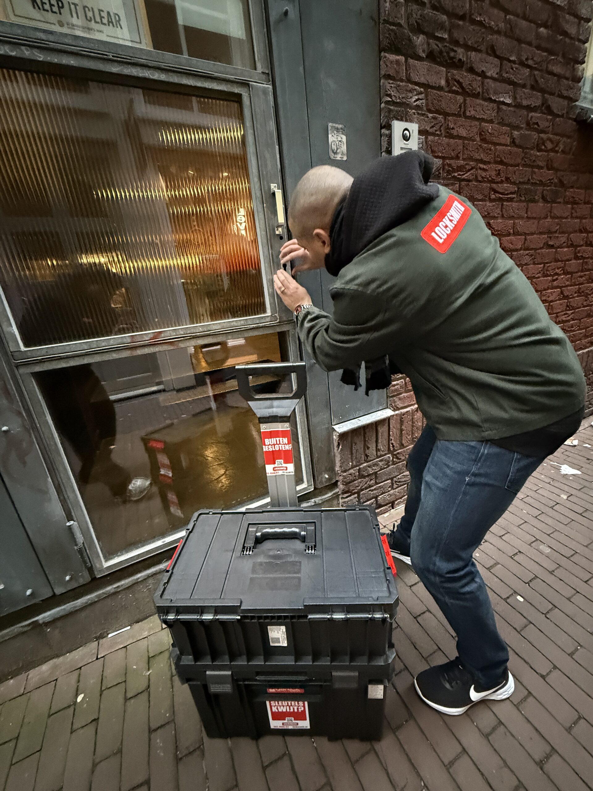 Slotenmaker opent deur met gereedschapskist nabij.