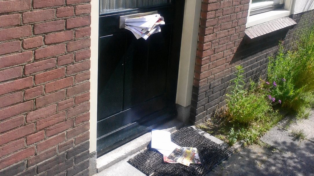 Voordeur van een Nederlandse rijtjeswoning met opgestapelde post in de brievenbus tijdens de zomervakantie