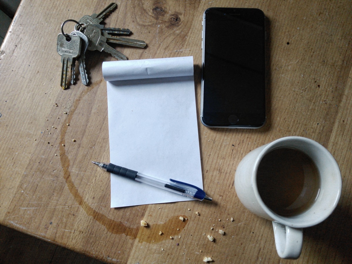 Telefoon, leeg notitieblok, pen en huissleutels op een houten keukentafel