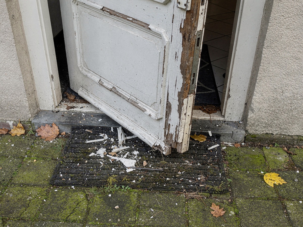 Dutch front door standing open after a break-in, with splintered wood around the lock and paint chips on the doormat